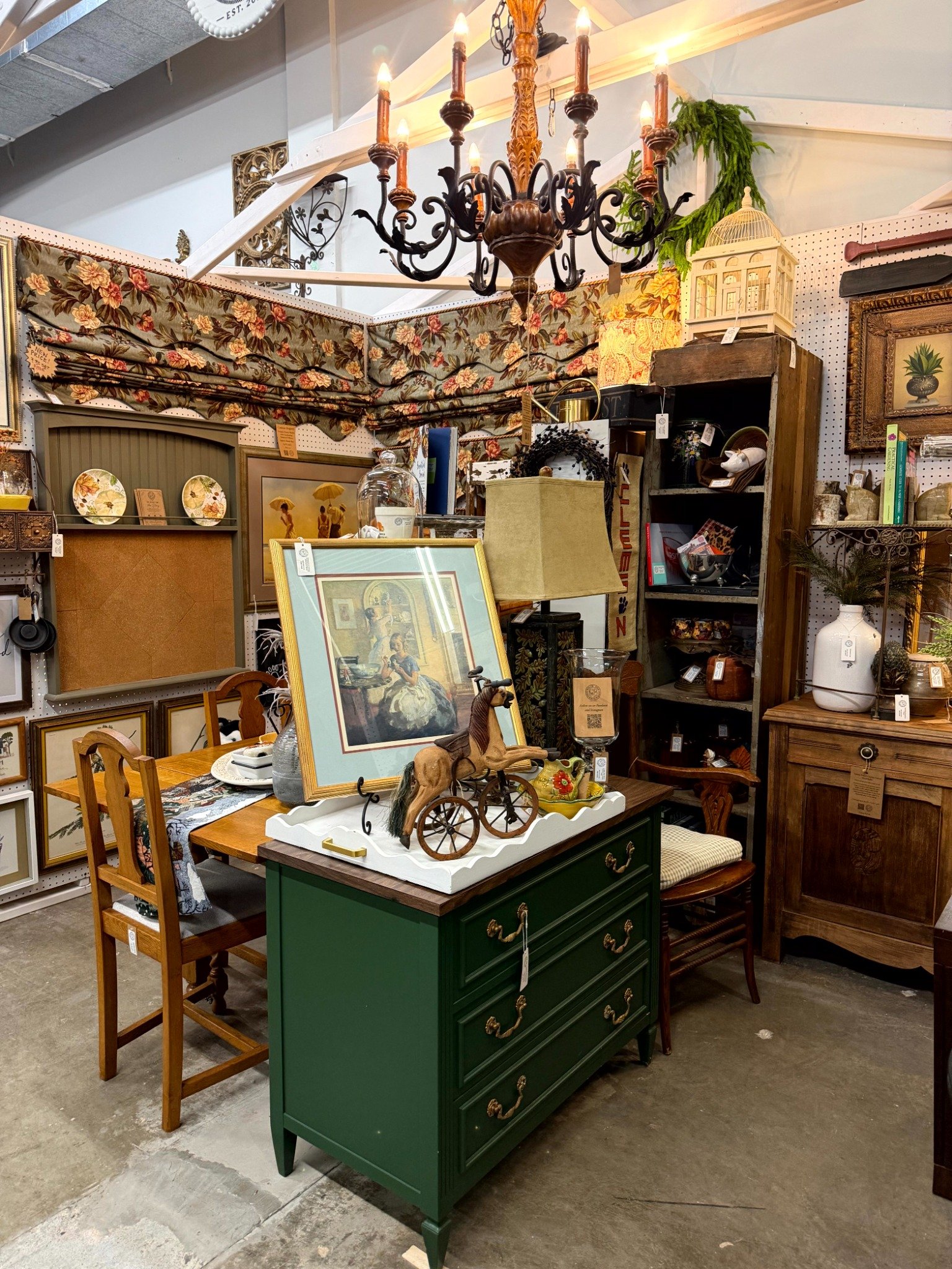 White Dog Haven’s vintage booth, with a chandelier, framed art, warm wood furniture, and a green chest of drawers.